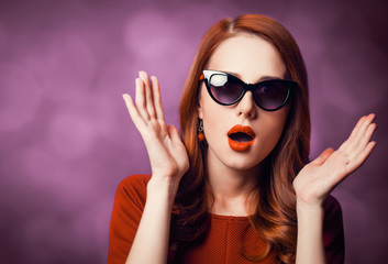 Beautiful redhead woman in sunglasses on viloet background.