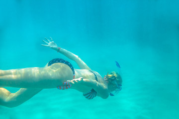 Female in apnea swims underwater with american flag bikini. Underwater background of a woman snorkeling and doing skin diving. Watersport activity in Hawaii. Tropical destination holiday concept.