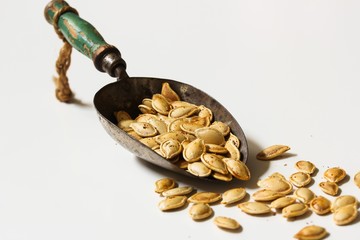 Baked pumpkin seeds in a metal scoop on white background
