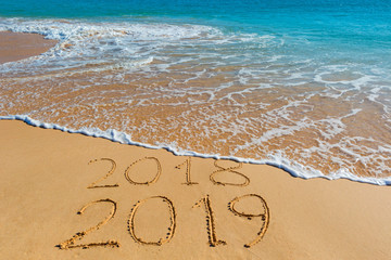 2018 2019 inscription written in the wet yellow beach sand being washed with sea water wave