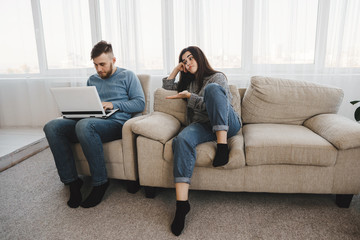 Obraz premium Bored couple ignore each other. Young people chatting online using smart phone and laptop. Internet and gadget addiction. Lack of communication, technology overuse.