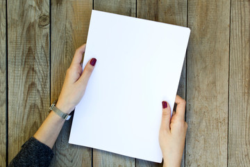 Woman hand holding blank paper on wooden table.