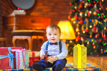 Fototapeta na wymiar funny baby sitting on the floor with a gift in hand on the background of a festive Christmas tree and smiling cheerfully