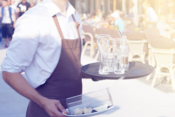 A waiter is holding a tray with dirty dishes and leftover food in a cafe on the beach. Waiter...
