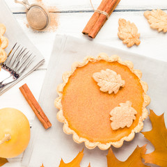 Pumpkin pie with cinnamon and cookies on gray napkins on white wooden background with autumn yellow leaves.