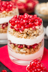 Pomegranate parfait - sweet organic layered dessert with granola flakes, yogurt and fruit seeds on black background.