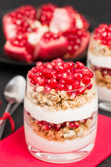 Pomegranate parfait - sweet organic layered dessert with granola flakes, yogurt and fruit seeds on black background.