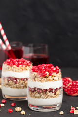 Pomegranate parfait - sweet organic layered dessert with granola flakes, yogurt and fruit seeds on black background.
