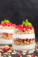 Pomegranate parfait - sweet organic layered dessert with granola flakes, yogurt and fruit seeds on black background.
