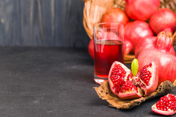 Ripe red pomegranates in wicker basket and seeds in spoon closeup photography on black background.