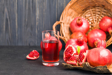 Ripe red pomegranates in wicker basket and seeds in spoon closeup photography on black background.