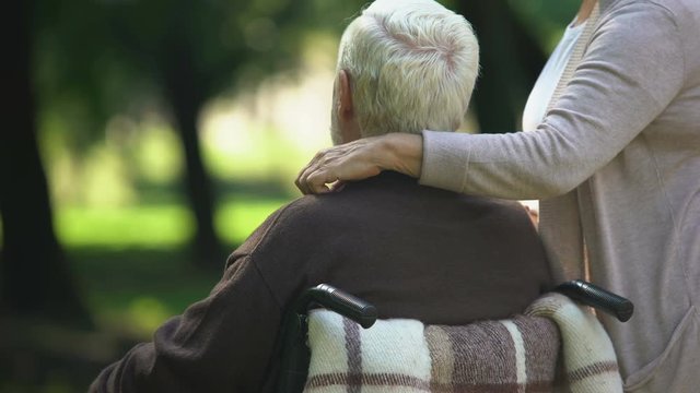 Wife supporting and comforting disabled husband in wheelchair, family care