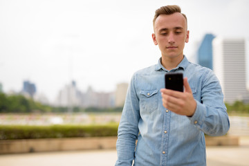 Young man with blond hair using mobile phone in park