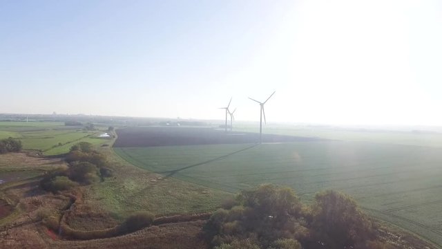 A sunny morning in Sweden. Wind power plants in the fields giving a slow moving shadow. Backwards drone shot with a river coming Ito frame.