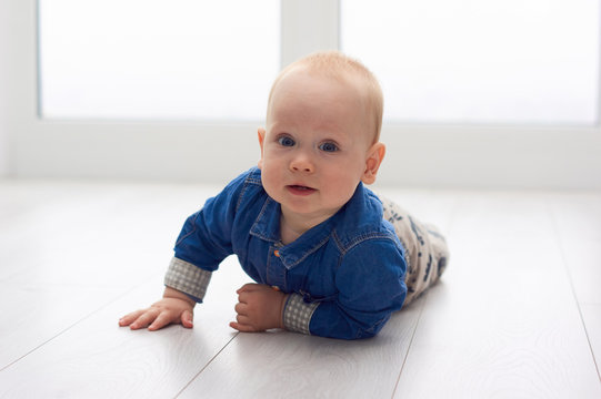 Portrait of a cute little baby in blue denim shirt laying on the floor. Candid image of young baby playing at home/Little baby play on the floor
