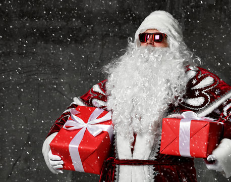 Santa Claus with red presents gifts for new year and sunglasses standing under snow
