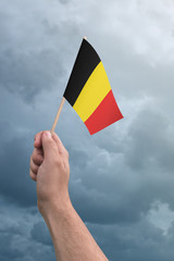 Hand holding Belgium flag high in the air, with a stormy, cloudy sky