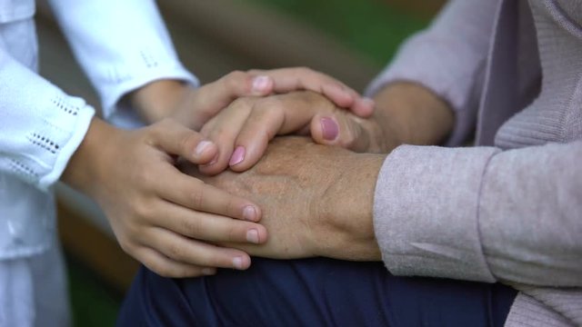Little girl gently stroking hands of her elderly grandmother, love and care