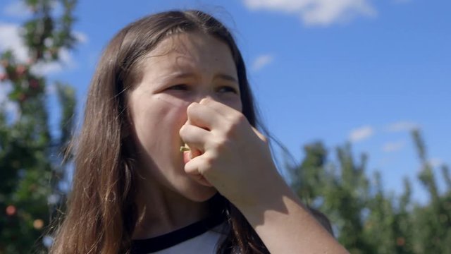 Cute little brown haired girl shows apple to camera and then takes a bite
