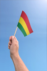 Fototapeta premium Hand holding Bolivia flag high in the air, with a clear blue sky