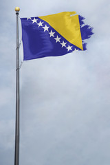 Worn and tattered Bosnia and Herzegovina flag blowing in the wind on a cloudy day
