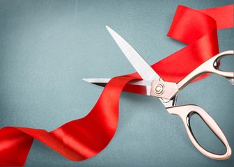 Scissors cutting red ribbon, close-up view on blue background