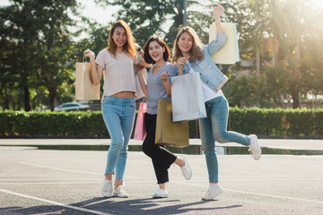Obraz premium Group of young Asian woman shopping in an outdoor market with shopping bags in their hands. Young Asian women show what they got in shopping bag under warm sunlight. Group outdoor shopping concept.