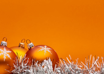 Three orange bauble Christmas decorations close up against an orange background with space for...