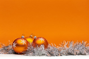 Three orange bauble Christmas decorations against an orange background with space for adding text.