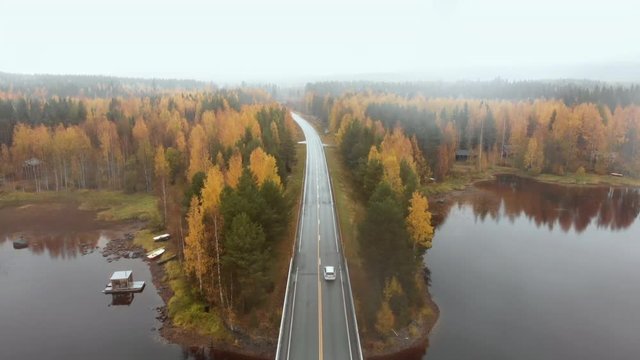 Aerial, drone shot, over car driving on a asphalt road,  bridge, surrounded by mist and autumn colors,, on a foggy, misty and cloudy, fall day, at lake Pielinen, in Nurmes, North Karelia, Finland