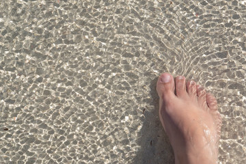 One female leg in the water. Sandy beach on the ocean