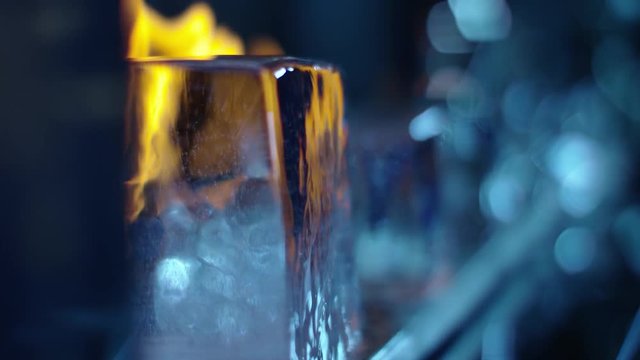Different geometrical large pieces of ice are on fire. The setting is 
a minimal bar with some colored glass pebbles. Shot on RED Raven 4.5K in 4K slowmotion.