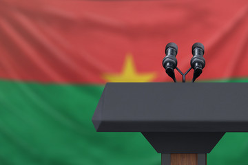 Podium lectern with two microphones and Burkina Faso flag in background