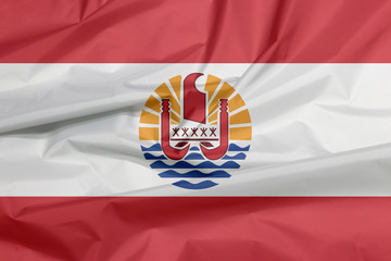 Fabric flag of French Polynesia. Crease of French Polynesia flag background. Two red horizontal and wide white; centered is a disk with Polynesian canoe rides on the wave.