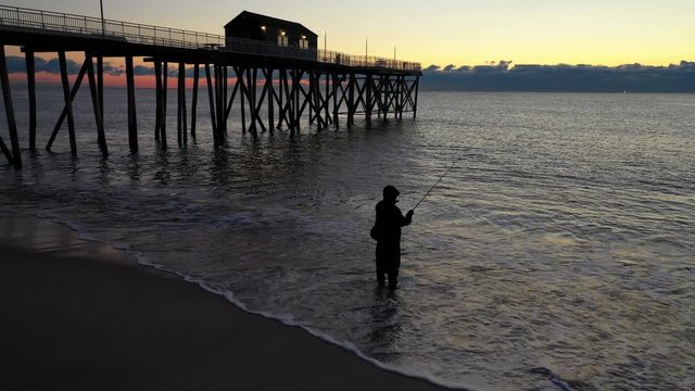 Man fishing at sunrise at Belmar beach, New Jersey.