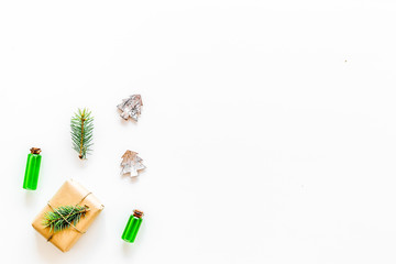 Composition with New Year gift wrapped in craft paper and decorted with pine sprout near pine sprigs, cones, spruce figure, fir oil on white background top view space for text