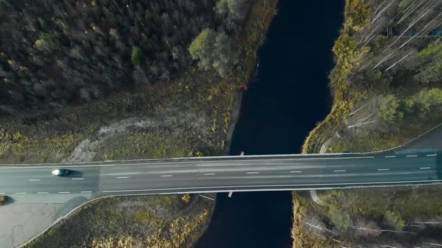 Aerial, top down, birdseye, drone shot, flying over a car driving over a bridge, between pine trees and leafless birch forest, on a cloudy, autumn day, in Juuka, North Karelia, ,Finland