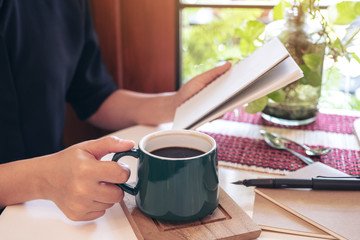 Closeup image of a woman holding notebook while drinking coffee in cafe