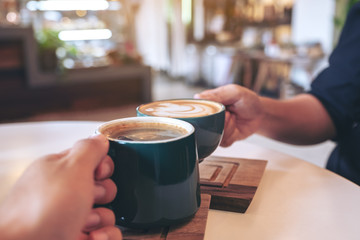 Close up image of a man and a woman clinking green coffee mugs in cafe