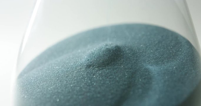 camera rotates slowly around the lower part of hour glass, showing the sand falling through in slow motion