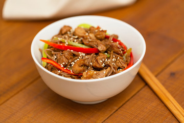 Noodles with pork, vegetables and sesame. On a wooden table.