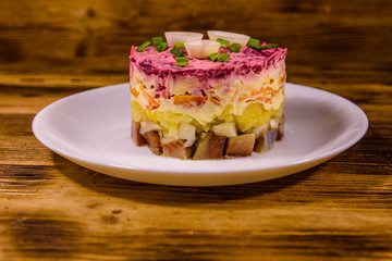 White plate with russian traditional new year salad herring under fur coat on wooden table