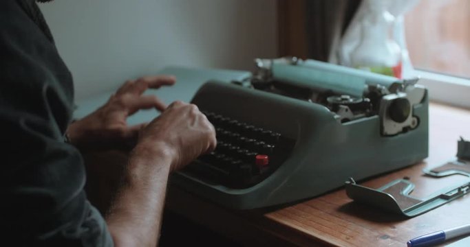 Close up of man typing on a type writer alone in a room.
