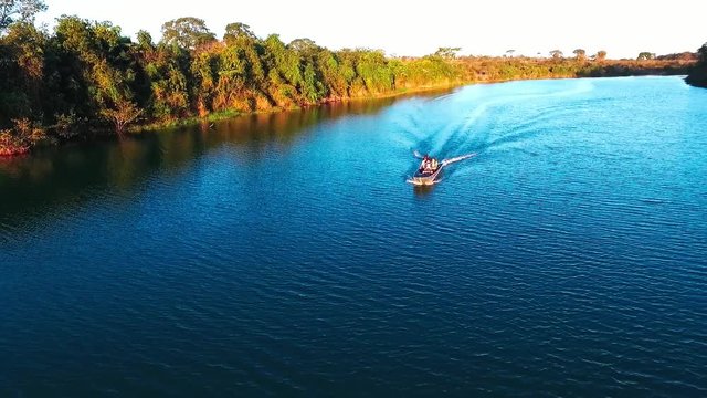 A small fishing boat travels down a deep blue river in the evening sun, aerial drone shot