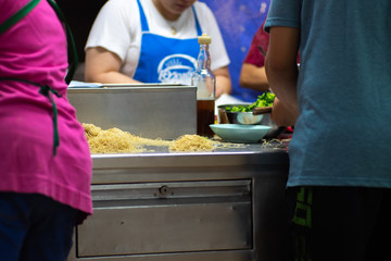 Closeup picture of noodle station in food market for cooking with blurred sellers