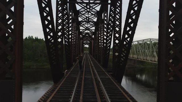 Girl walking on train rails leading through a bridge over a majestic river