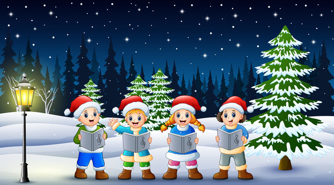 Children singing christmas carols in winter chlotes and santa hat with snowy pine background