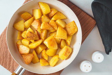 Top view on roasted potato in a white pan on a kitchen table. Modern style, vegetarian food.