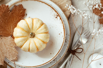 Top view on a decorated table setting for Thanksgiving dinner. Autumn ornate, white pumpkin on...