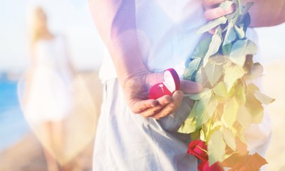 Man hiding bouquet of roses from woman at seaside
